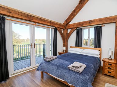 A bedroom with a bed covered with a blue blanket and towels on it two bedside tables with lamps wooden beams and glass doors opening to a balcony at Yr Adfa Llangeitho near Tregaron