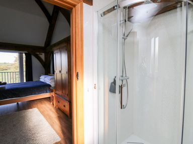 A bedroom with wooden furniture and a bed viewed through a doorway from a bathroom with a glass shower at Yr Adfa in Llangeitho near Tregaron