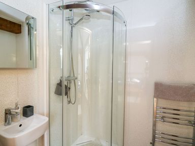 A bathroom with a glass corner shower enclosure a white sink with a faucet a mirror cabinet above the sink and a chrome towel rack with a towel at Yr Adfa Llangeitho near Tregaron