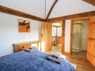 A bedroom with a blue bedspread and folded towels on the bed a wooden dresser with a mirror and an open door leading to a bathroom with a shower at Yr Adfa in Llangeitho near Tregaron