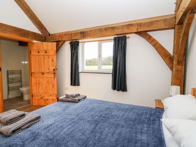 A bedroom with wooden beams blue bedspread on the bed and an open door leading to a bathroom at Yr Adfa in Llangeitho near Tregaron