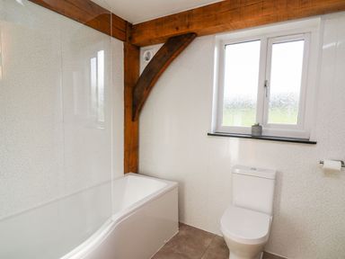 A bathroom with a bathtub a toilet a window with a small plant and wooden beams at Yr Adfa in Llangeitho near Tregaron