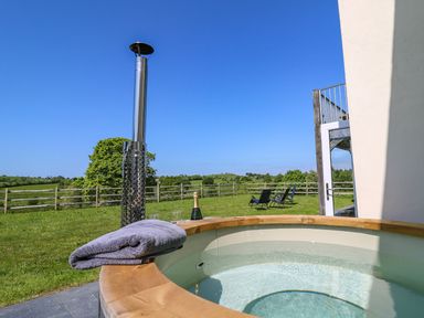 An outdoor hot tub with a towel on the edge and a chiminea with grass and chairs in the background at Yr Adfa in Llangeitho near Tregaron