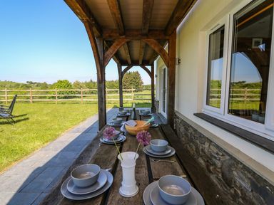 An outdoor wooden dining table with plates bowls and flowers under a covered patio at Yr Adfa in Llangeitho near Tregaron