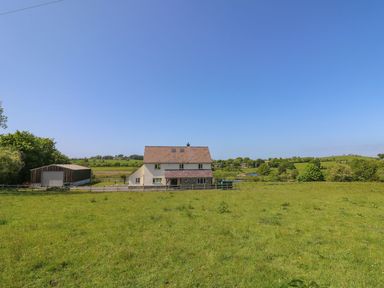 A house with a pitched roof and an adjacent large shed in a grassy field with trees and hills at Yr Adfa in Llangeitho near Tregaron