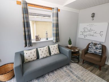 A living room with a sofa and armchair next to a window with curtains and a table with a plant and coasters on it at Chalet 22 in Port Eynon