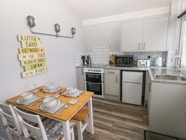 A kitchen with dining table set for four next to a countertop with microwave toaster kettle and stove at Chalet 22 in Port Eynon