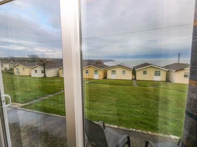 A view of small houses with grass lawn and a path outside a window at Chalet 22 in Port Eynon