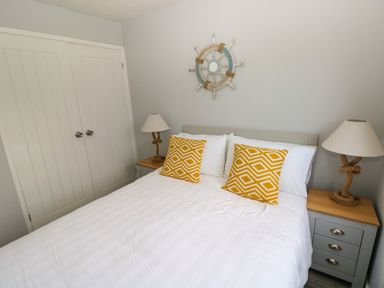 A bedroom with a bed with two yellow patterned pillows two bedside tables with lamps and a wall decoration above the headboard at Chalet 22 in Port Eynon
