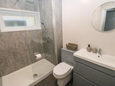 A bathroom with a shower area toilet sink with soap dispensers and a round mirror at Chalet 22 in Port Eynon