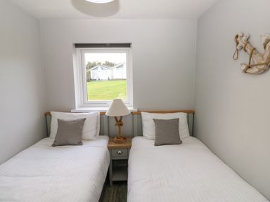 A bedroom with two single beds separated by a nightstand with a lamp under a window and a decorative anchor on the wall at Chalet 22 in Port Eynon