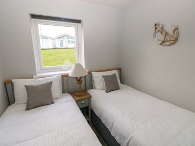 A bedroom with two single beds separated by a nightstand with a lamp and a window above the beds at Chalet 22 in Port Eynon