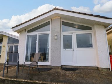 The front exterior of a small house with two outdoor chairs on a concrete patio at Chalet 22 in Port Eynon