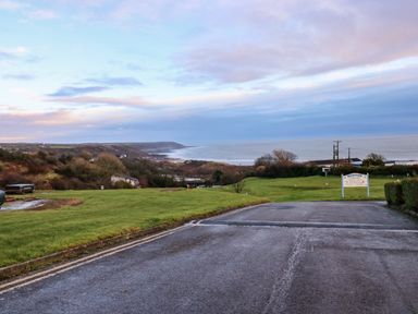 A coastal view with a paved road leading to grassy areas and a sign near the ocean at Chalet 22 in Port Eynon