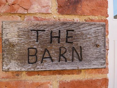 A wooden sign with the words THE BARN on a brick wall at Home Farm Barn in Todenham near Moreton-In-Marsh