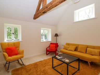A living room with a yellow sofa yellow chair with orange cushions and a red chair around a glass coffee table at Home Farm Barn in Todenham near Moreton-In-Marsh