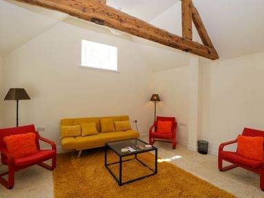 A living room with a yellow sofa red armchairs a black glass coffee table and wooden beams at Home Farm Barn Todenham near Moreton-In-Marsh