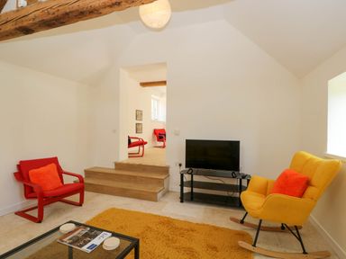 A living room with a yellow rocking chair red chairs a television on a stand and a rug at Home Farm Barn Todenham near Moreton-In-Marsh