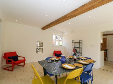 A dining room with a black table set with dishes and glasses yellow and blue chairs and red armchairs at Home Farm Barn in Todenham near Moreton-In-Marsh