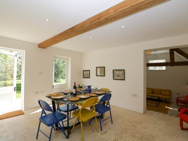 A dining room with a black table set with plates and glasses and colorful chairs in front of a door at Home Farm Barn in Todenham near Moreton In Marsh