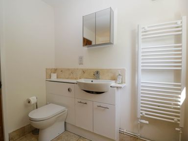 A bathroom with a toilet sink cabinet mirror and towel radiator at Home Farm Barn in Todenham near Moreton-In-Marsh