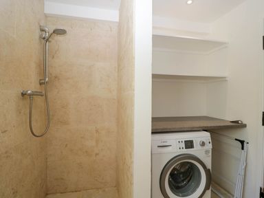 A bathroom with a shower next to a laundry area with a washing machine and shelves at Home Farm Barn in Todenham near Moreton-In-Marsh