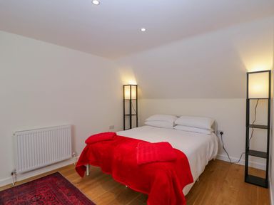 A bedroom with a double bed red blanket bedside lamps and a radiator on wooden floor at Home Farm Barn Todenham near Moreton-In-Marsh
