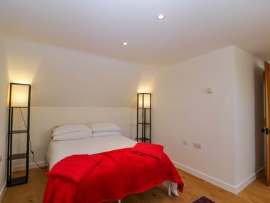 A bedroom with a double bed with white bedding and red blanket between two black floor lamps at Home Farm Barn in Todenham near Moreton-In-Marsh