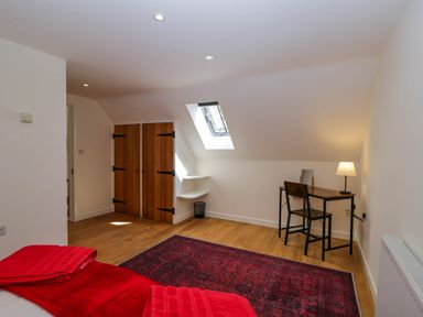 A bedroom with a wooden desk and chair near a skylight window and wooden double doors at Home Farm Barn in Todenham near Moreton-In-Marsh