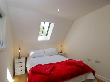 A bedroom with a double bed covered in white linens and red blankets under a skylight window at Home Farm Barn in Todenham near Moreton-In-Marsh