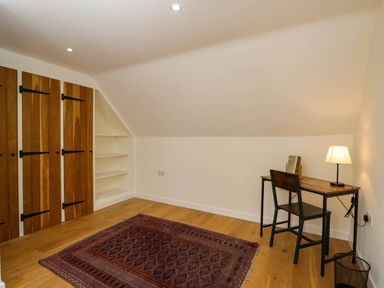 A room with wooden wardrobes a desk with a chair and lamp and a rug on the wooden floor at Home Farm Barn in Todenham near Moreton-In-Marsh