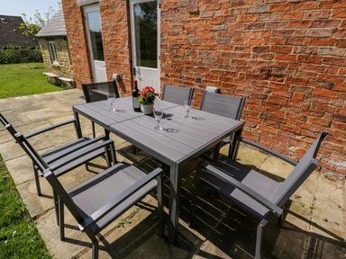 An outdoor patio with a gray table and six chairs four glasses a bottle of wine and a potted plant at Home Farm Barn Todenham near Moreton-In-Marsh