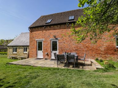 An outdoor patio with a table and six chairs in front of a red brick building at Home Farm Barn in Todenham near Moreton-In-Marsh
