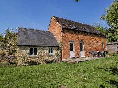 An exterior view of a brick and stone house with a patio and outdoor dining set at Home Farm Barn Todenham near Moreton-In-Marsh