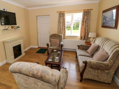 A living room with a sofa and two armchairs a coffee table a fireplace a wall-mounted TV and a window at Robin's Roost 2 in Cornamona County Galway