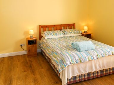 A bedroom with a double bed a patterned bedspread two bedside tables with lamps and wooden flooring at Robin's Roost 2 in Cornamona County Galway