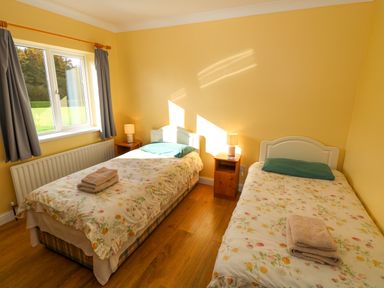 A bedroom with two single beds with floral bedspreads and towels on top next to a window with curtains and wooden floor at Robin's Roost 2 in Cornamona County Galway