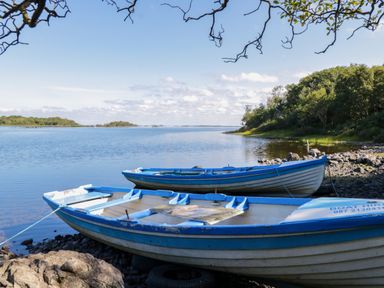 Two blue and white boats on rocky shore of a calm lake with trees and islands in the background at Robins Roost 2 in Cornamona County Galway