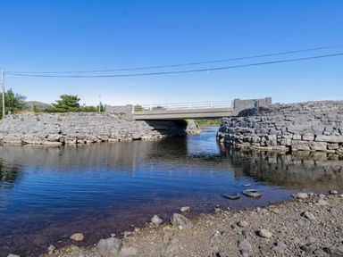 A stone bridge over water with rocky banks and a clear blue sky at Robins Roost 2 in Cornamona County Galway