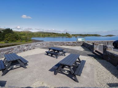 An outdoor seating area with three picnic tables and a stone wall overlooking a lake and trees at Robins Roost 2 Cornamona County Galway