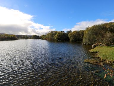 A body of water with trees on the banks under a partly cloudy sky at Robins Roost 2 in Cornamona County Galway