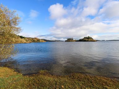 A lake with small islands and trees under a partly cloudy sky at Robin's Roost 2 in Cornamona County Galway