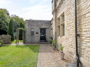 A stone building entrance with a black door potted plants along a brick pathway and tall trees in the background at Walworth Castle Lodge in Walworth near Darlington