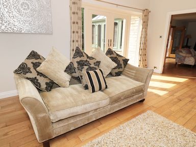 A beige sofa with multiple cushions in front of glass doors with curtains at Walworth Castle Lodge in Walworth near Darlington
