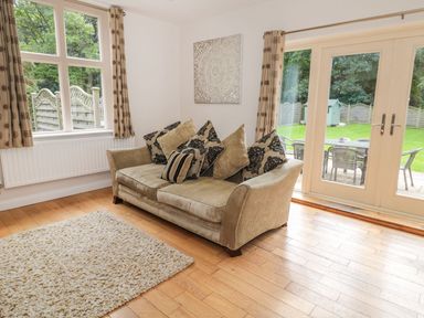 A living room with a beige sofa and cushions next to windows and glass doors showing a garden at Walworth Castle Lodge in Walworth near Darlington