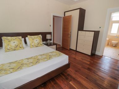 A bedroom with a bed and bedside table with lamp a wardrobe and chest of drawers wooden floor and an open door showing a bathroom at Walworth Castle Lodge in Walworth near Darlington