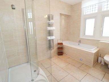 A bathroom with a shower enclosure, a bathtub, towel rack, shelving unit, and two windows at Walworth Castle Lodge Walworth near Darlington