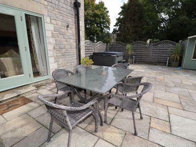 An outdoor patio with a stone table and six wicker chairs near a house at Walworth Castle Lodge in Walworth near Darlington