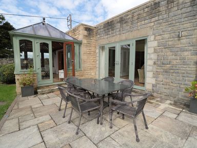 An outdoor patio with a glass table and six wicker chairs next to a stone house with green framed doors at Walworth Castle Lodge in Walworth near Darlington