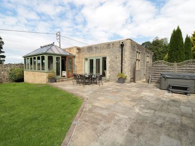 A stone patio with outdoor dining set and hot tub beside a building with green framed windows and a conservatory at Walworth Castle Lodge in Walworth near Darlington